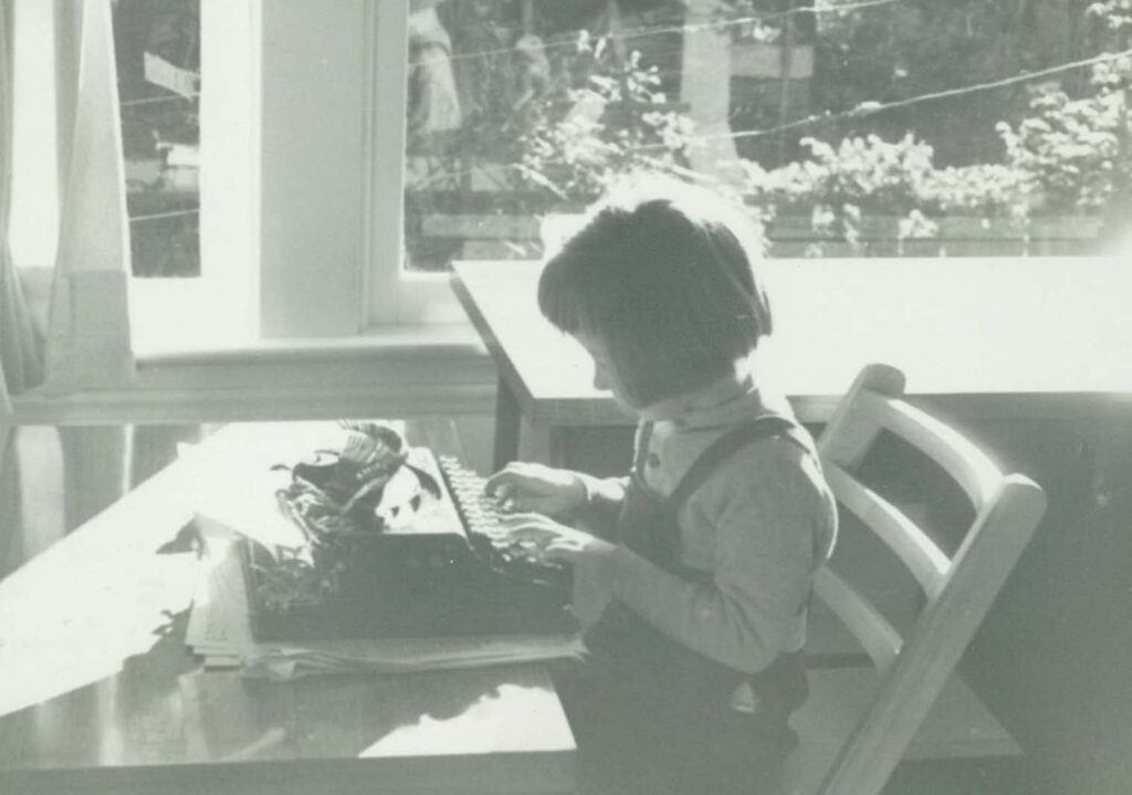 Little girl sitting at a table with a typewriter in black and white